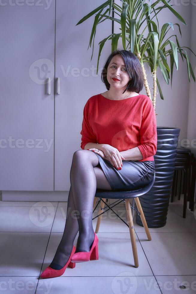 portrait of a brunette with a bob haircut in a red sweater and a leather mini skirt in the office photo