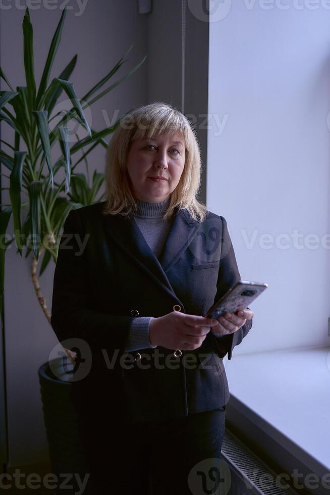 retrato de un rubia medio años mujer en un negocio traje en el oficina foto