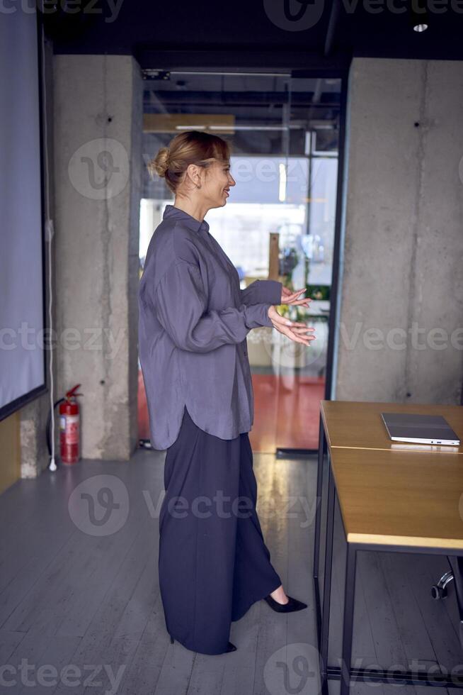 un hermosa negocio mujer Hablando a un reunión en frente de un grande proyector pantalla foto