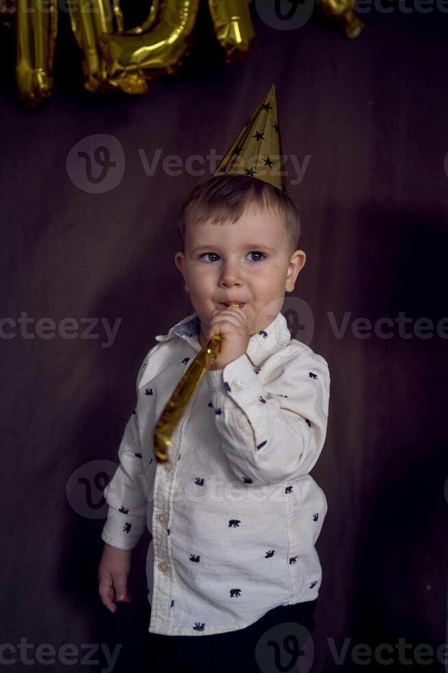 a toddler in a party cap blows a whistle flute photo