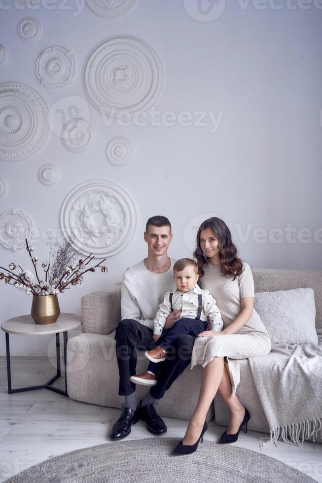 hermosa familia sentado en sofá con su pequeño chico en minimalista estudio foto