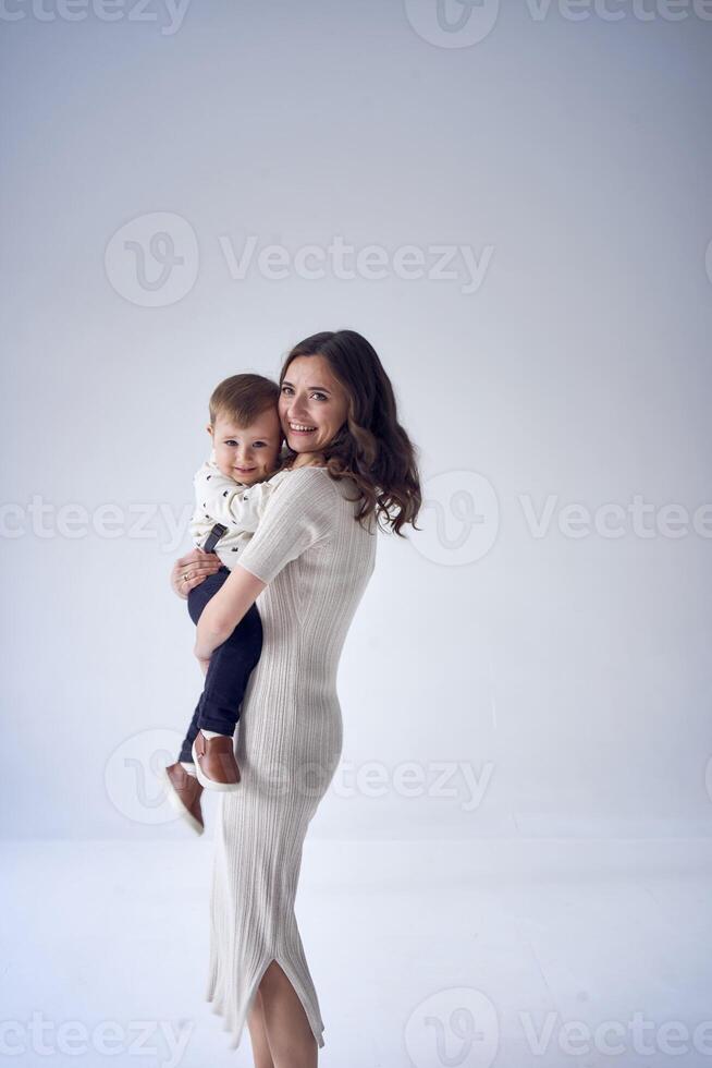 beautiful mother holds her son in her arms in a minimalistic studio photo