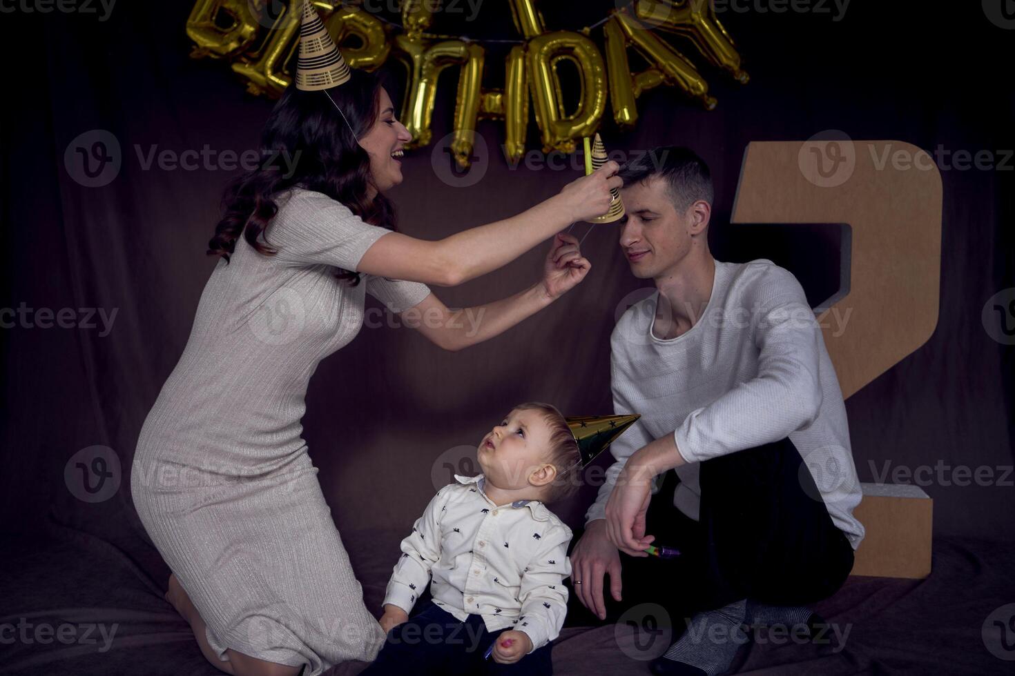 family celebrating toddler's birthday wearing party hats blowing pipes photo