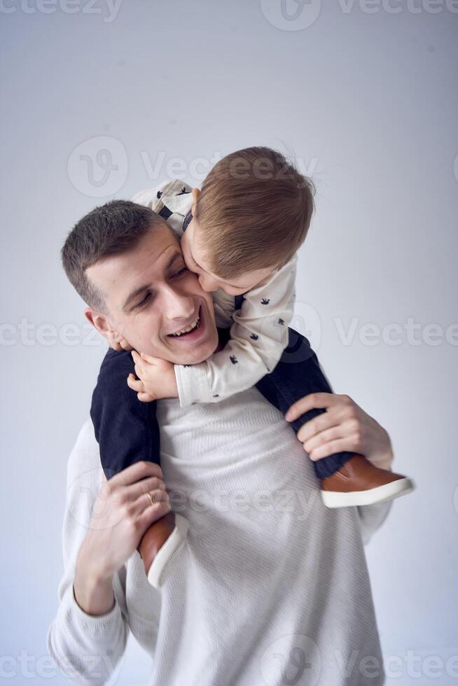 un padre lleva su hijo en su brazos y obras de teatro con él en un minimalista estudio foto