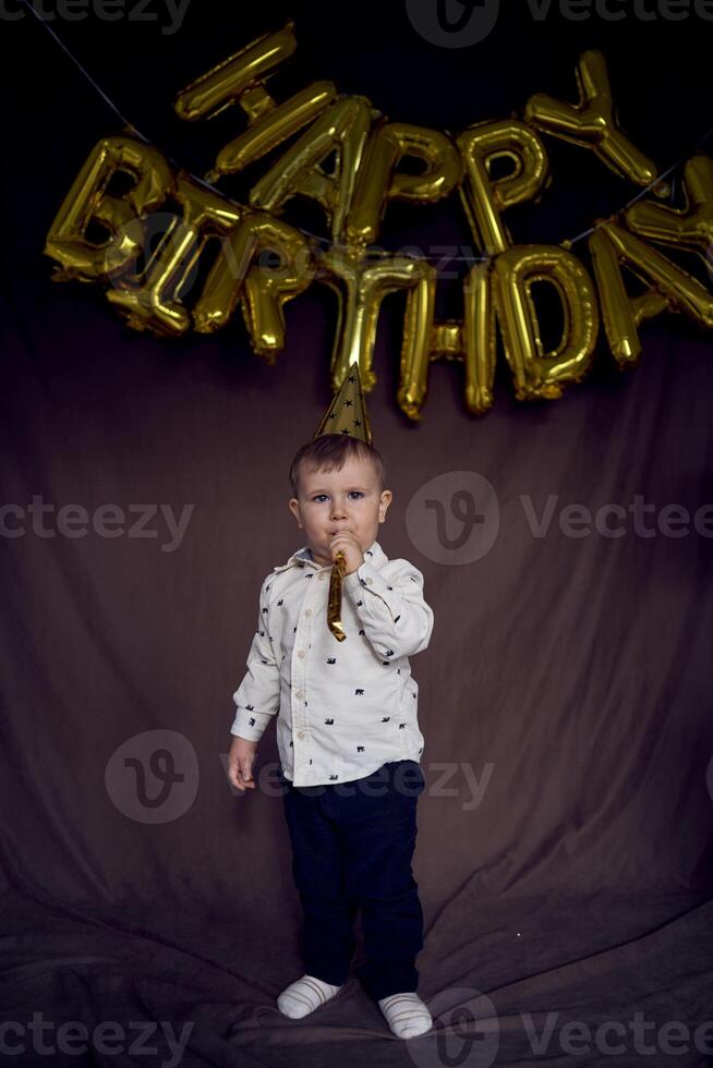 a toddler in a party cap blows a whistle flute photo