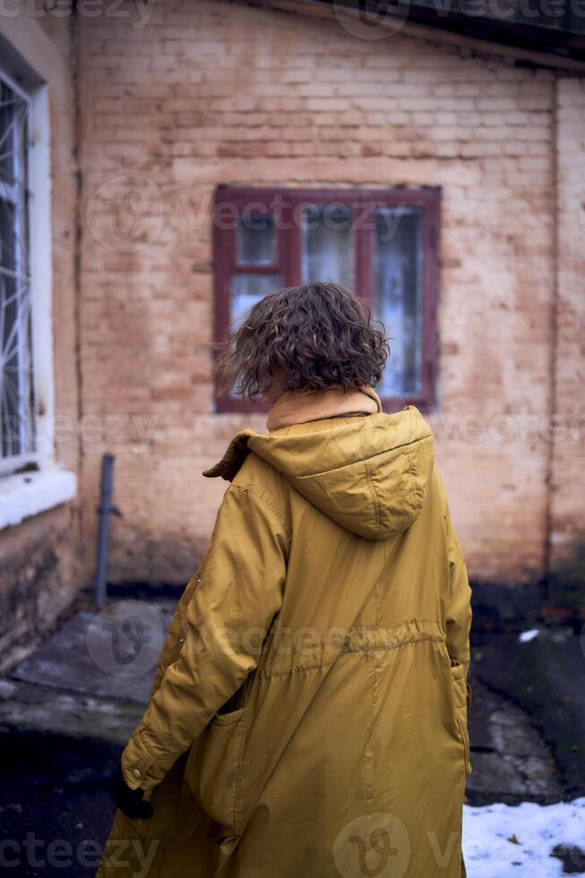 woman in yellow coat in front of brick building photo