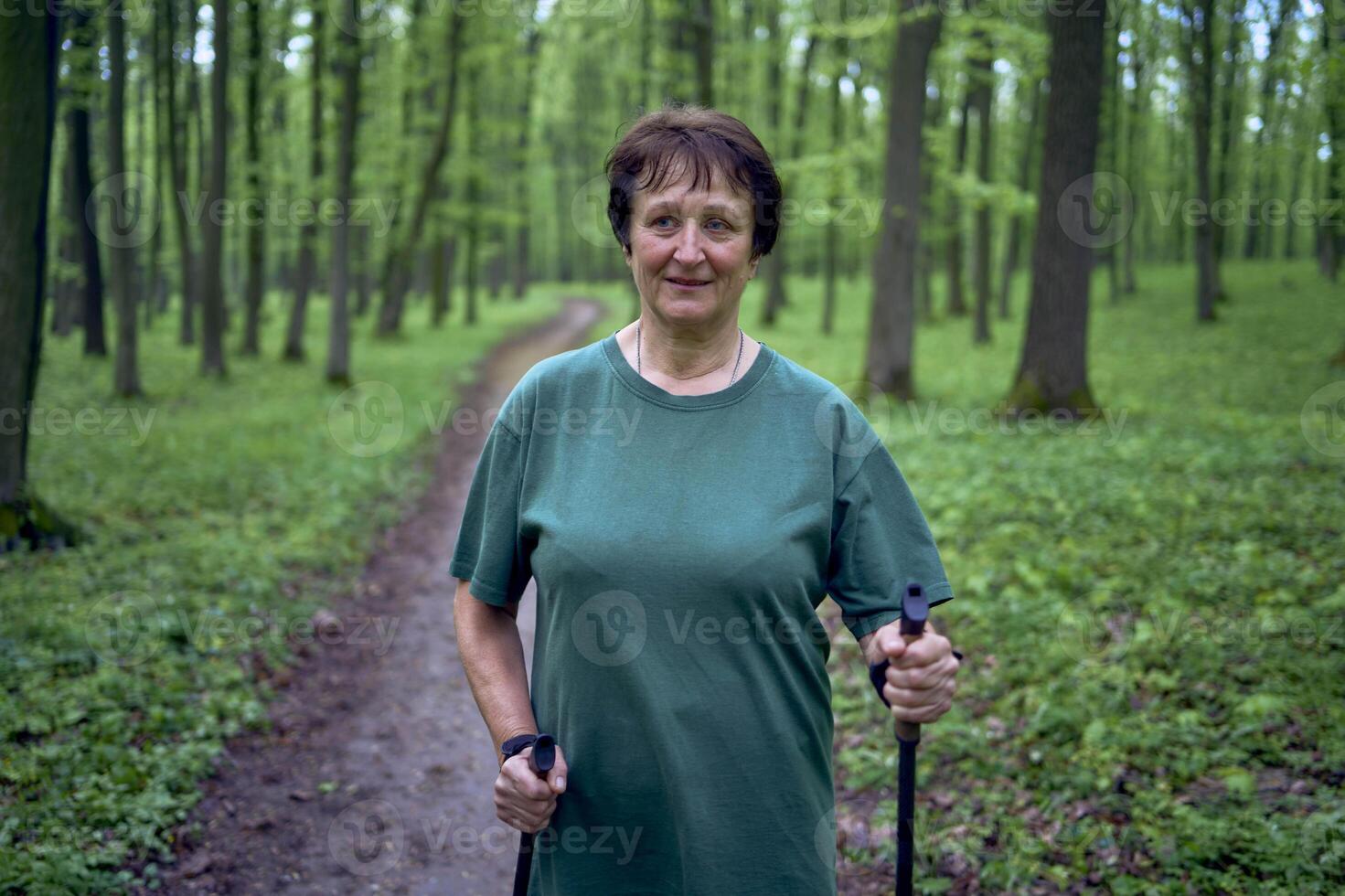 elderly woman is engaged in Nordic walking with sticks in the spring forest photo