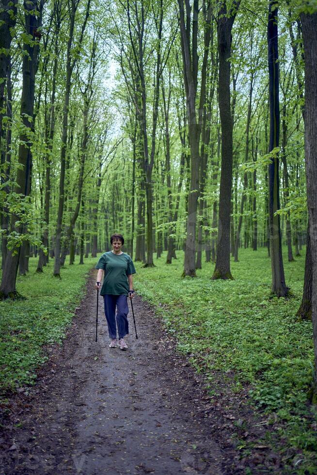 mayor mujer es comprometido en nórdico caminando con palos en el primavera bosque foto