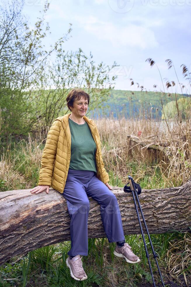 elderly woman rests on the river bank after Nordic walking exercise photo