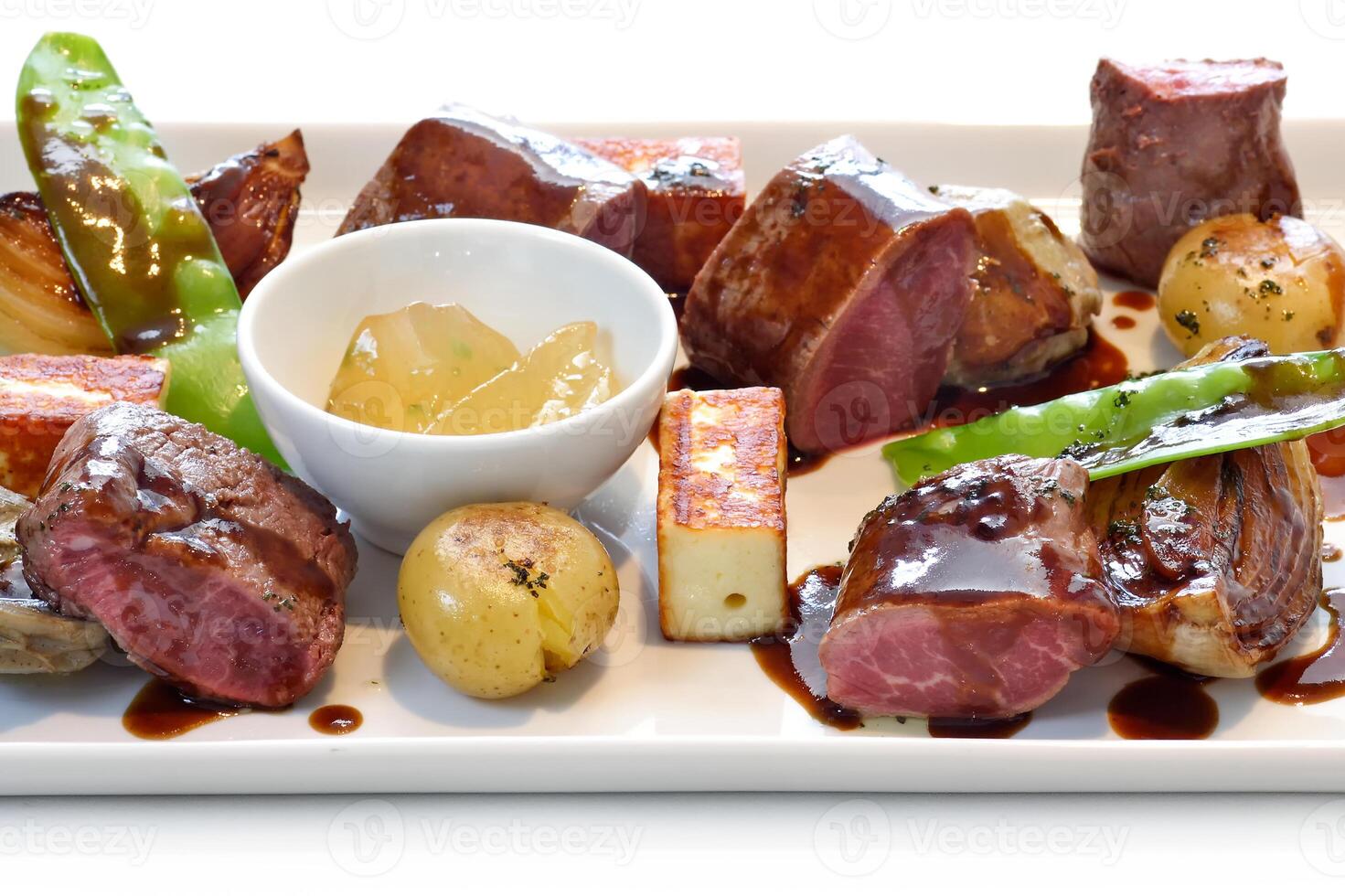 dish with various meats, grilled cheese and vegetables accompanied by a jar of apricot jam photo