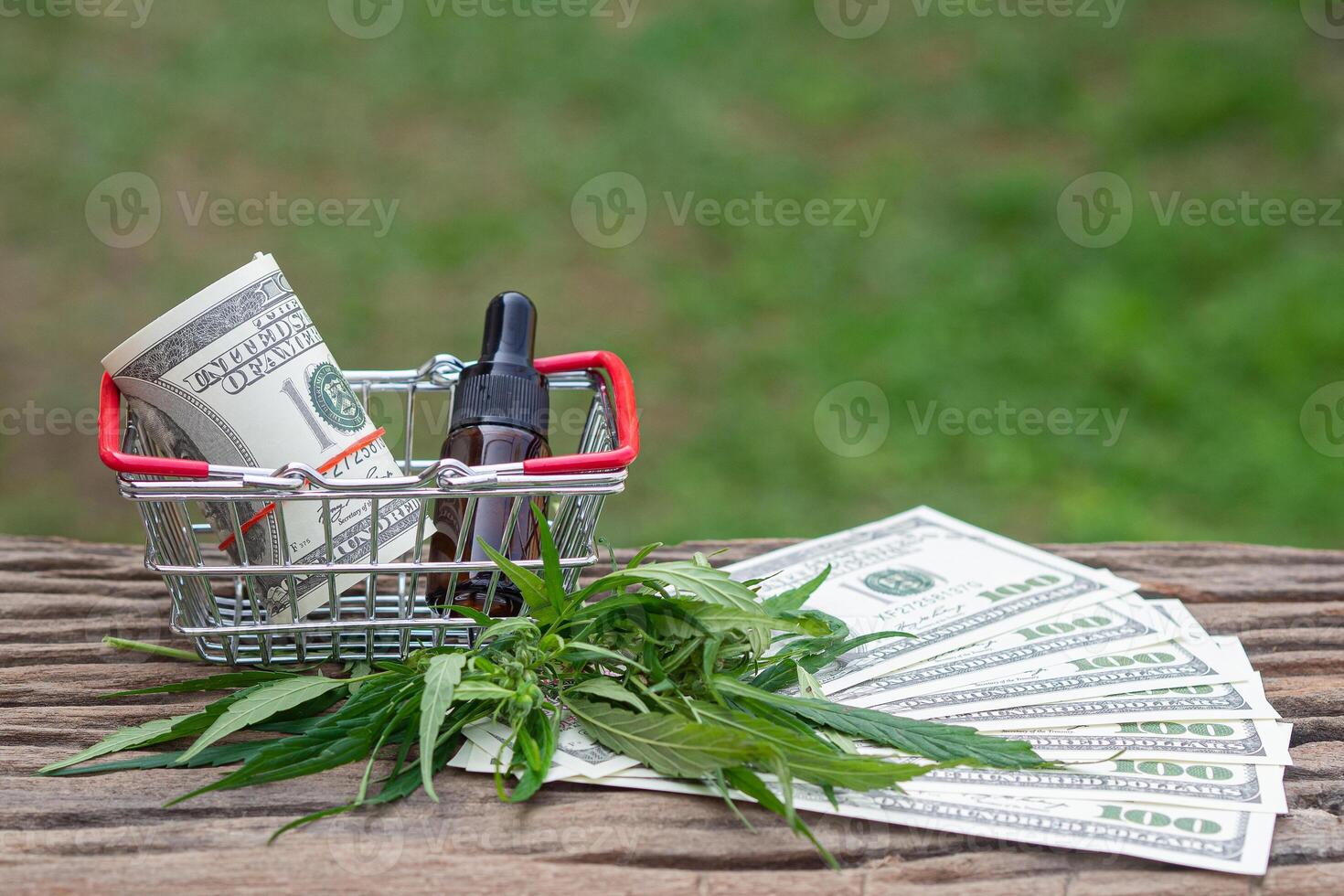 Roll of US dollars and cannabis oil extracts in a jar placed on the shopping cart with cannabis leaves, money dollars on a wooden table. CBD hemp oil from natural marijuana. Space for text photo