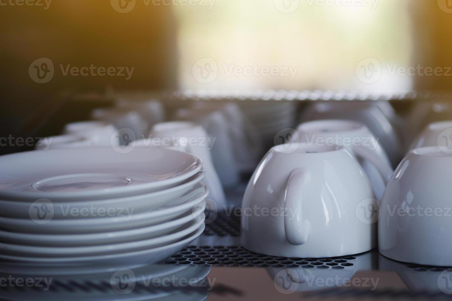 de cerca de un blanco café tazas y platillos son metido al revés abajo en parte superior de el café fabricante con luz de sol antecedentes foto