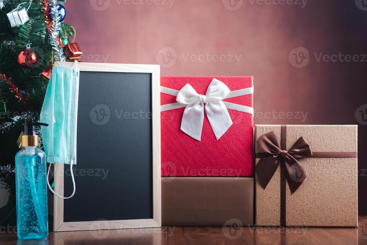 Small blackboard, mask, alcohol gel, and gift boxes on wooden table with a Christmas tree and vintage wall background. Space for text. Concept of Christmas, new year festival and healthcare photo