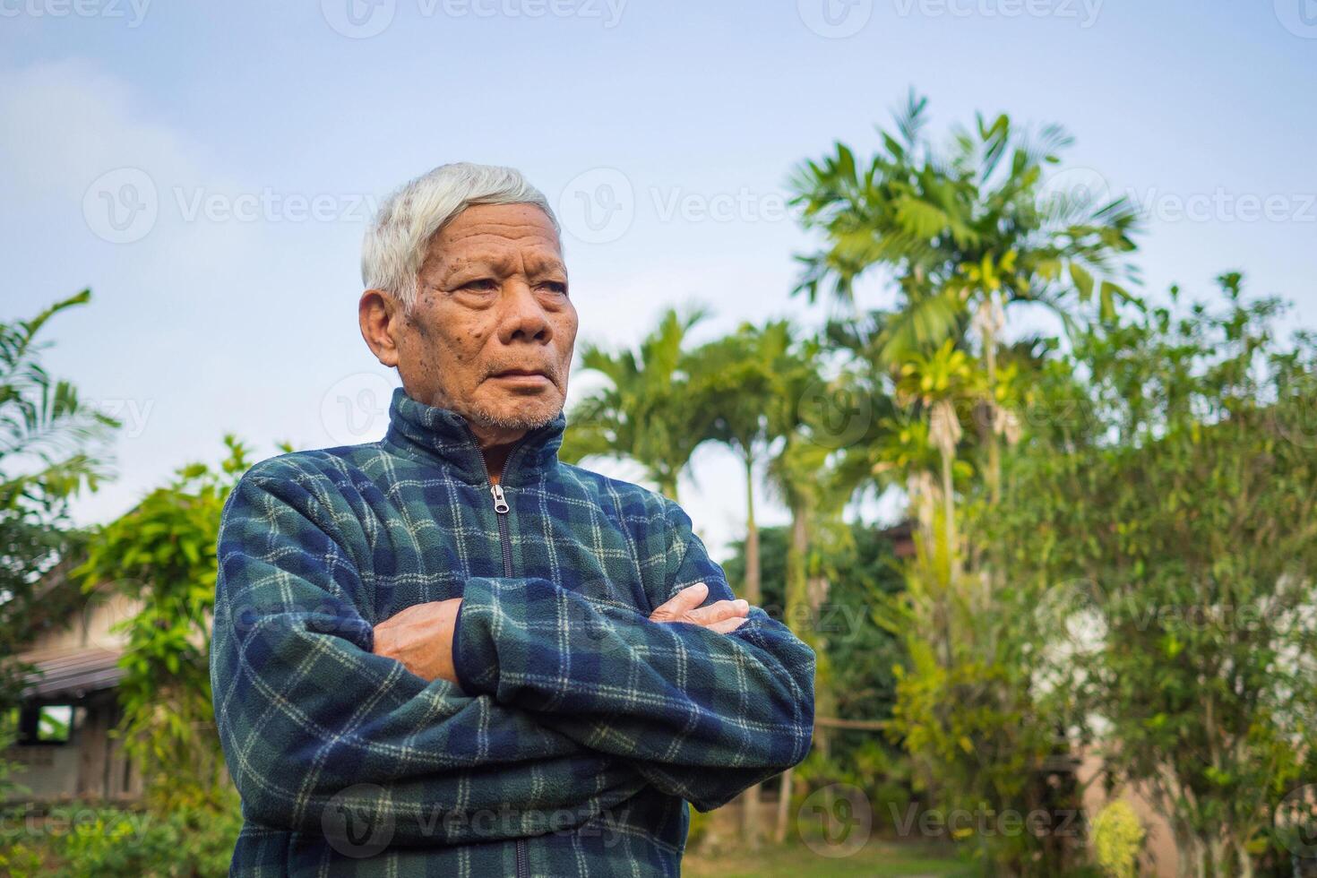 Portrait of elderly Asian man arms crossed standing and looking away while standing in a garden. Space for text. Concept of aged people and healthcare photo