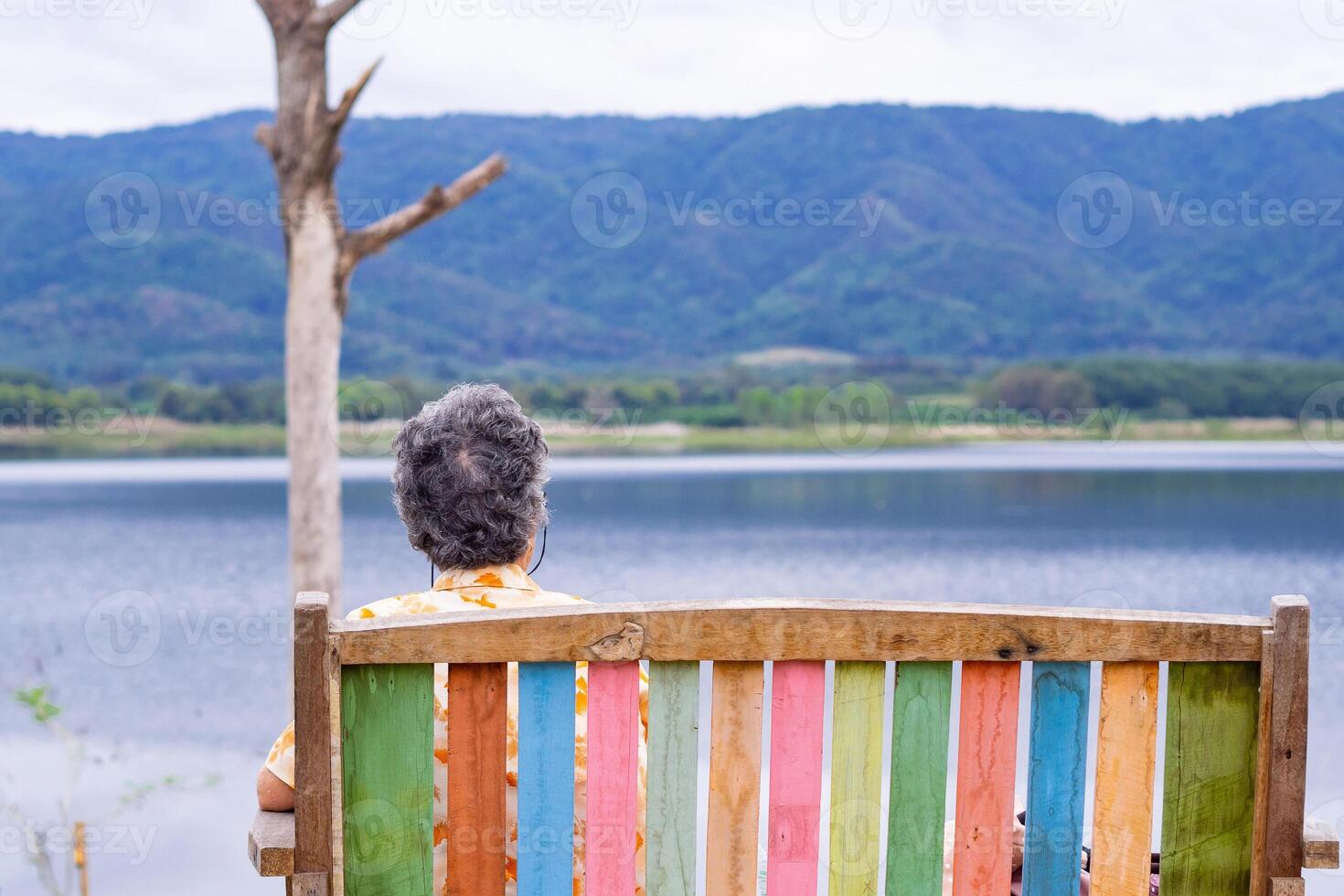 Back view of a senior woman sitting on chair side the lake. Space for text. Concept of aged people and relaxation photo
