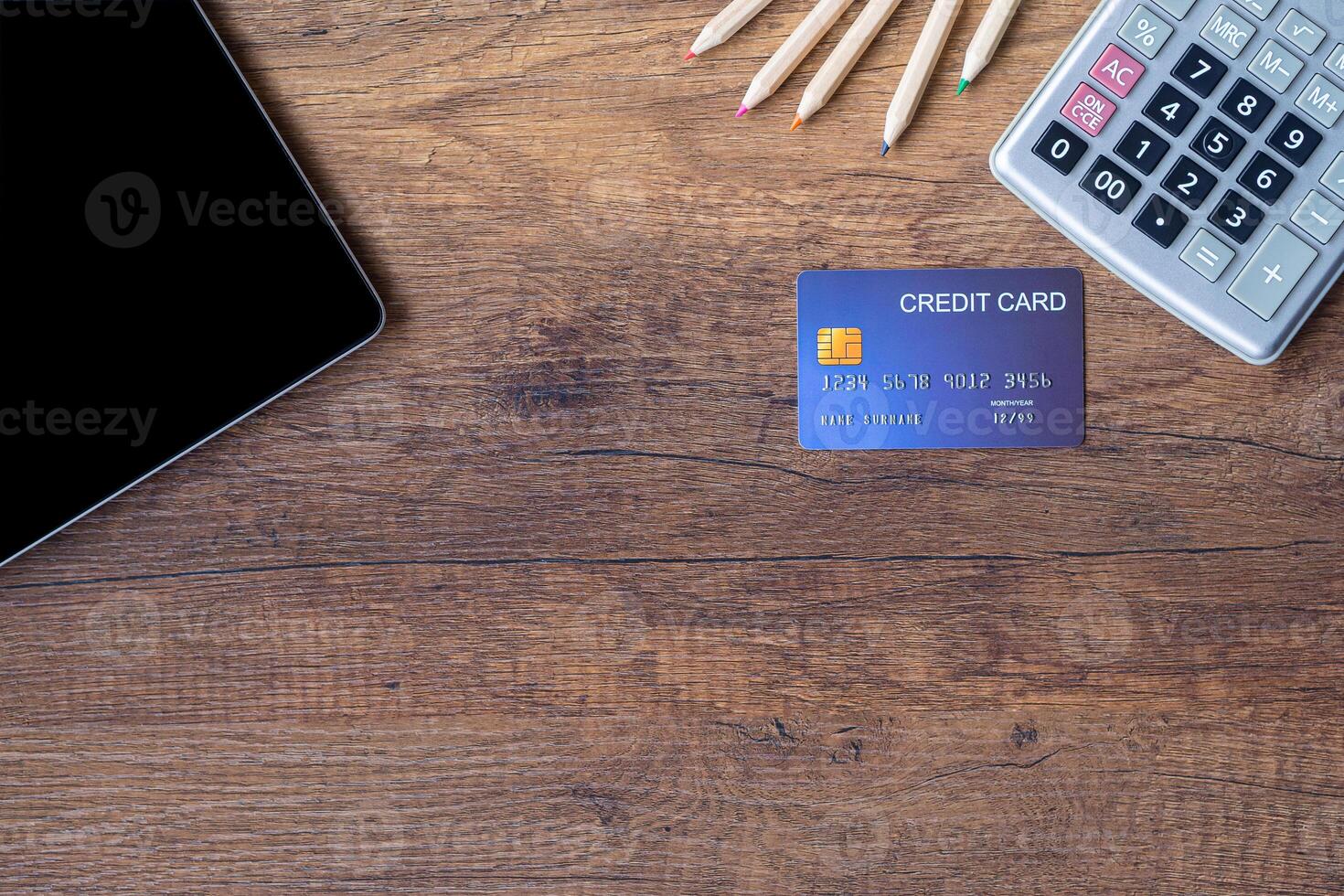 Top view of a blue credit card, pencil, calculator, and tablet on wooden table in the office. Space for text. Wood texture background. Business and finance concept photo