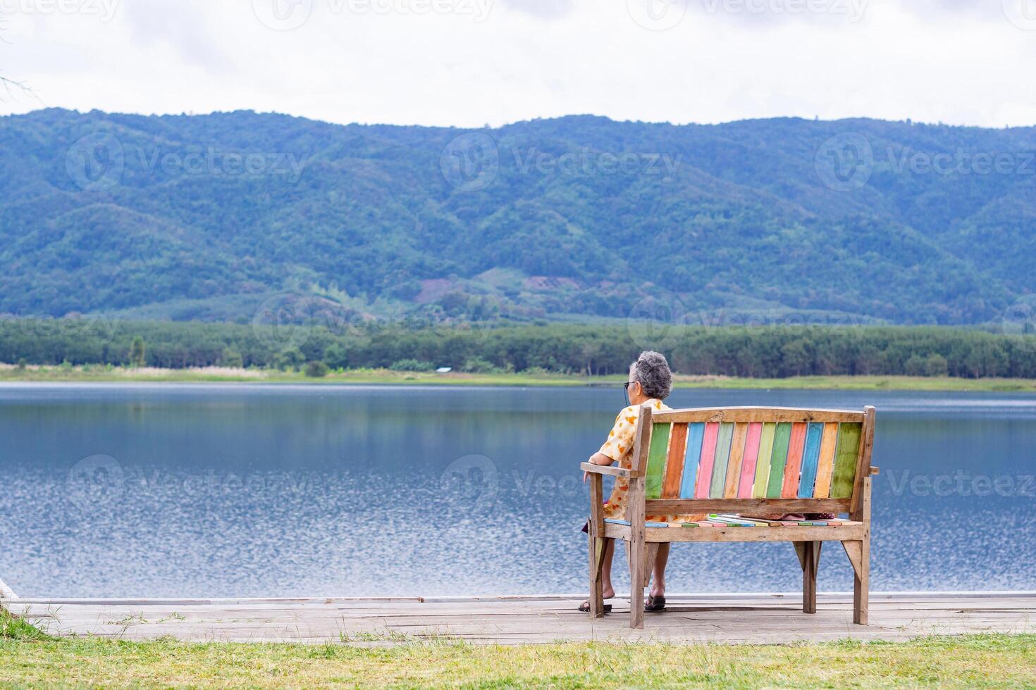 Back view of a senior woman sitting on chair side the lake. Space for text. Concept of aged people and relaxation photo