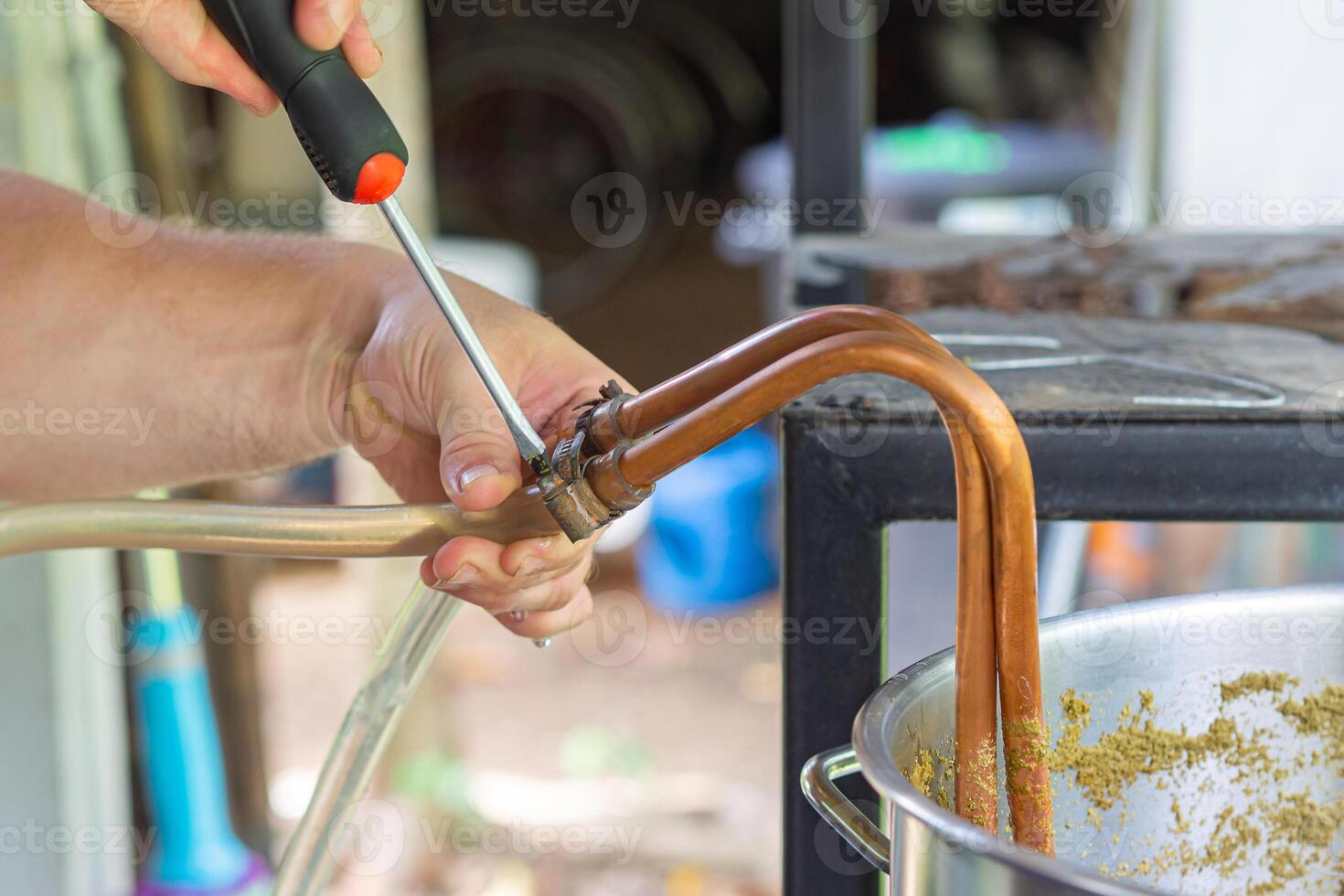 de cerca de manos joven del hombre participación un destornillador a apretar el caucho Correa a dejar el arte cerveza fluir afuera. selectivo enfocar. hogar fabricación de cerveza proceso foto