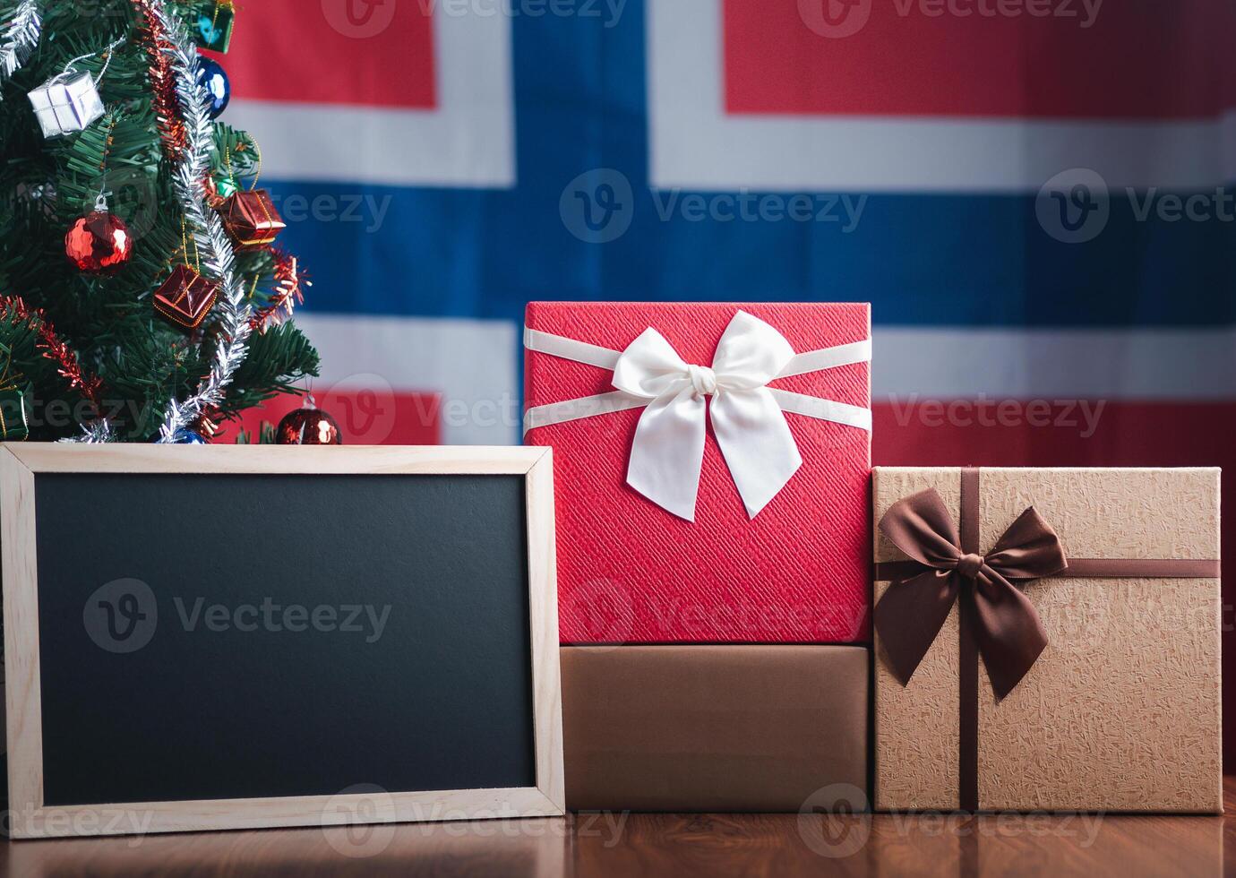 Small blackboard and gift boxes on wooden table with a Christmas tree and Norway flag in the background. Space for text. Concept of Christmas and new year festival photo