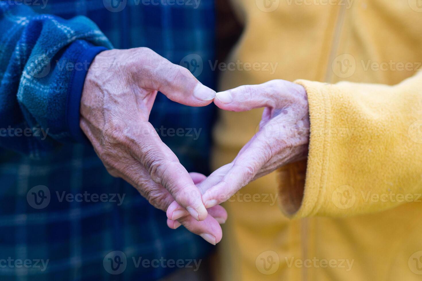 Close-up of the elderly couple's hand showing a heart-shaped symbol with fingers. Concept of aged people and love photo