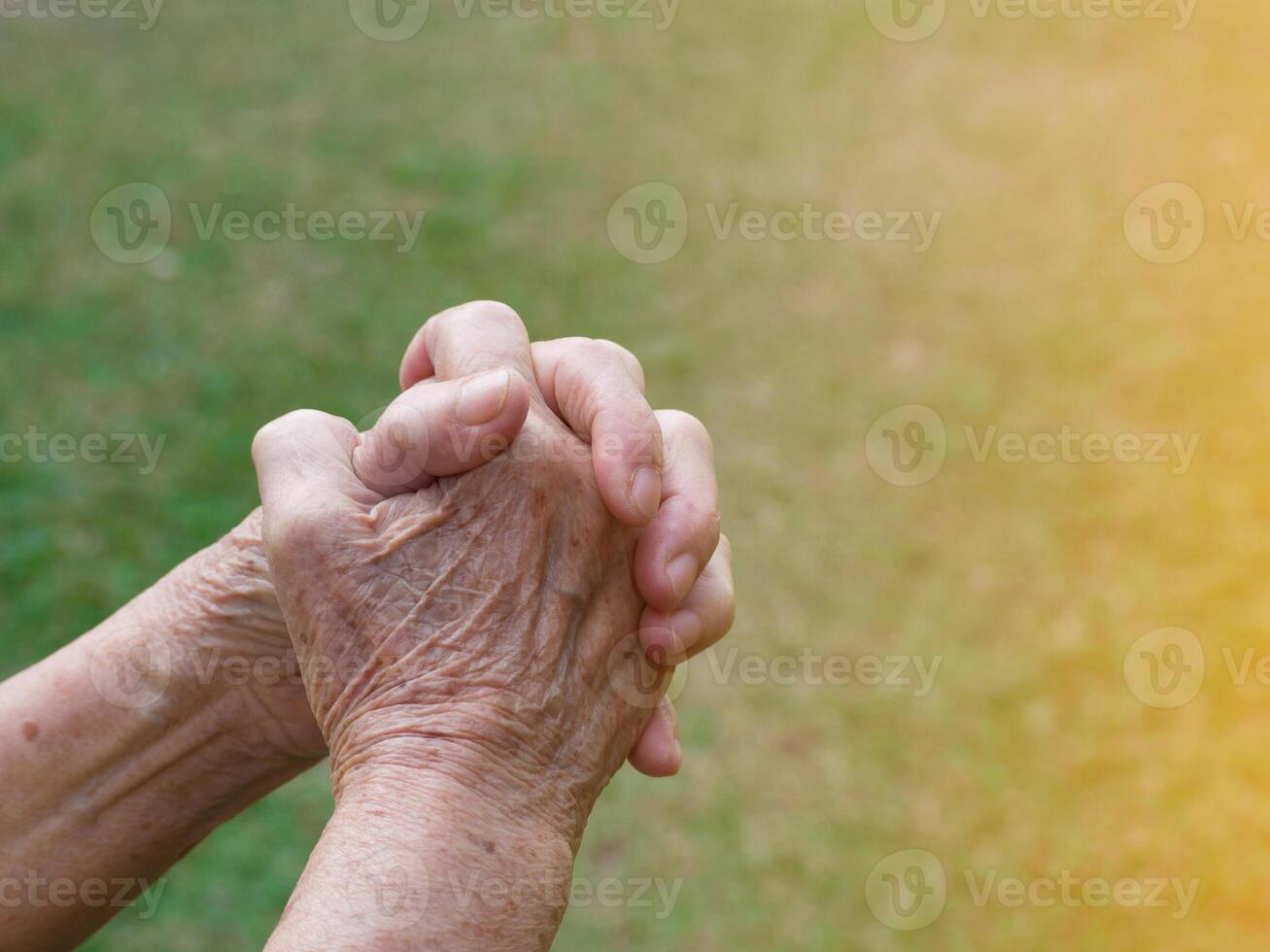 Close-up of senior woman's hands praying to god with sunlight at the garden. Space for text. Concept of aged people and hope photo