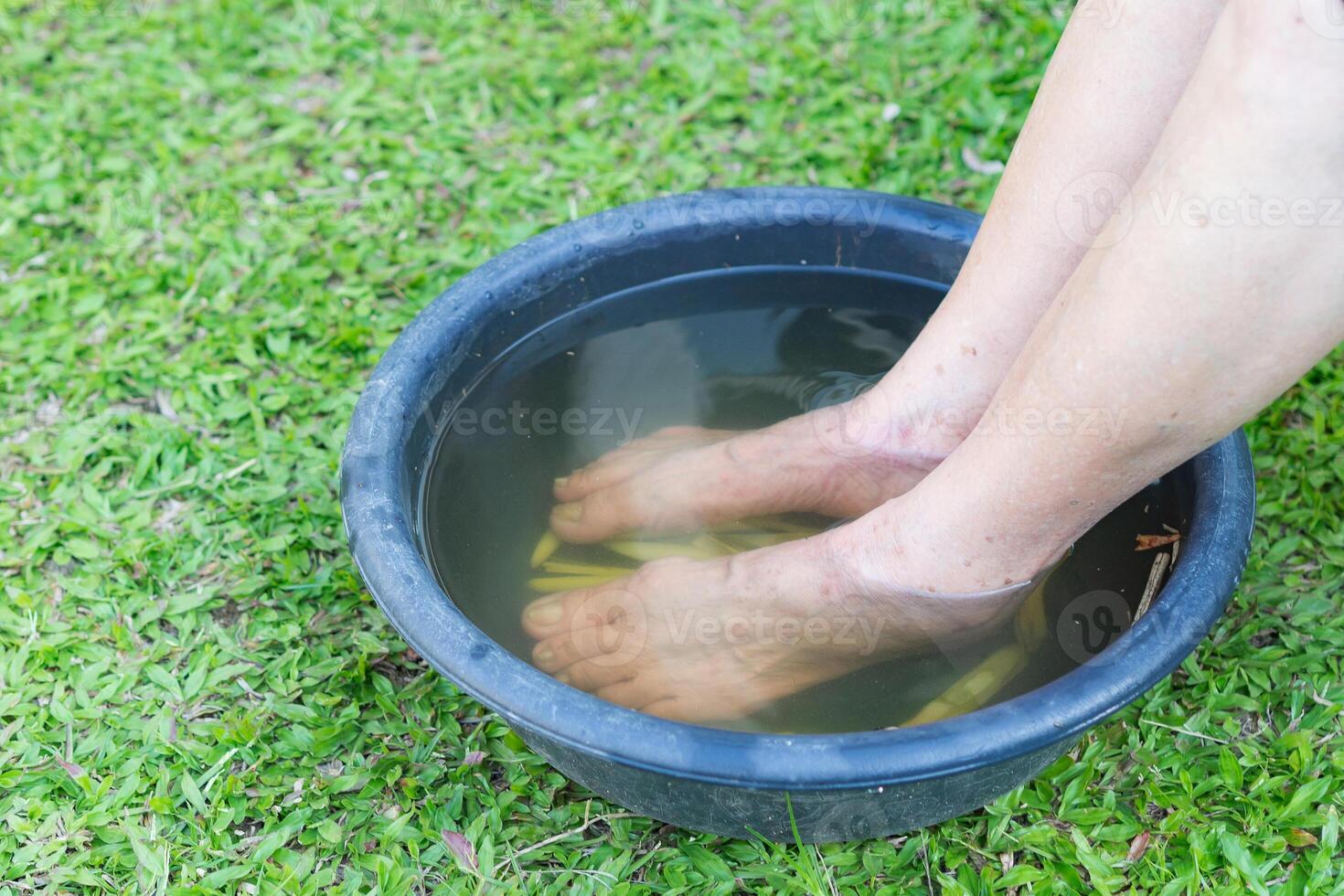 Close-up of spa foot with herbs water for relaxation treatment. A senior woman with ankle pain uses herbal treatment to relax the muscles by soaking warm water that is boiled from herbs photo