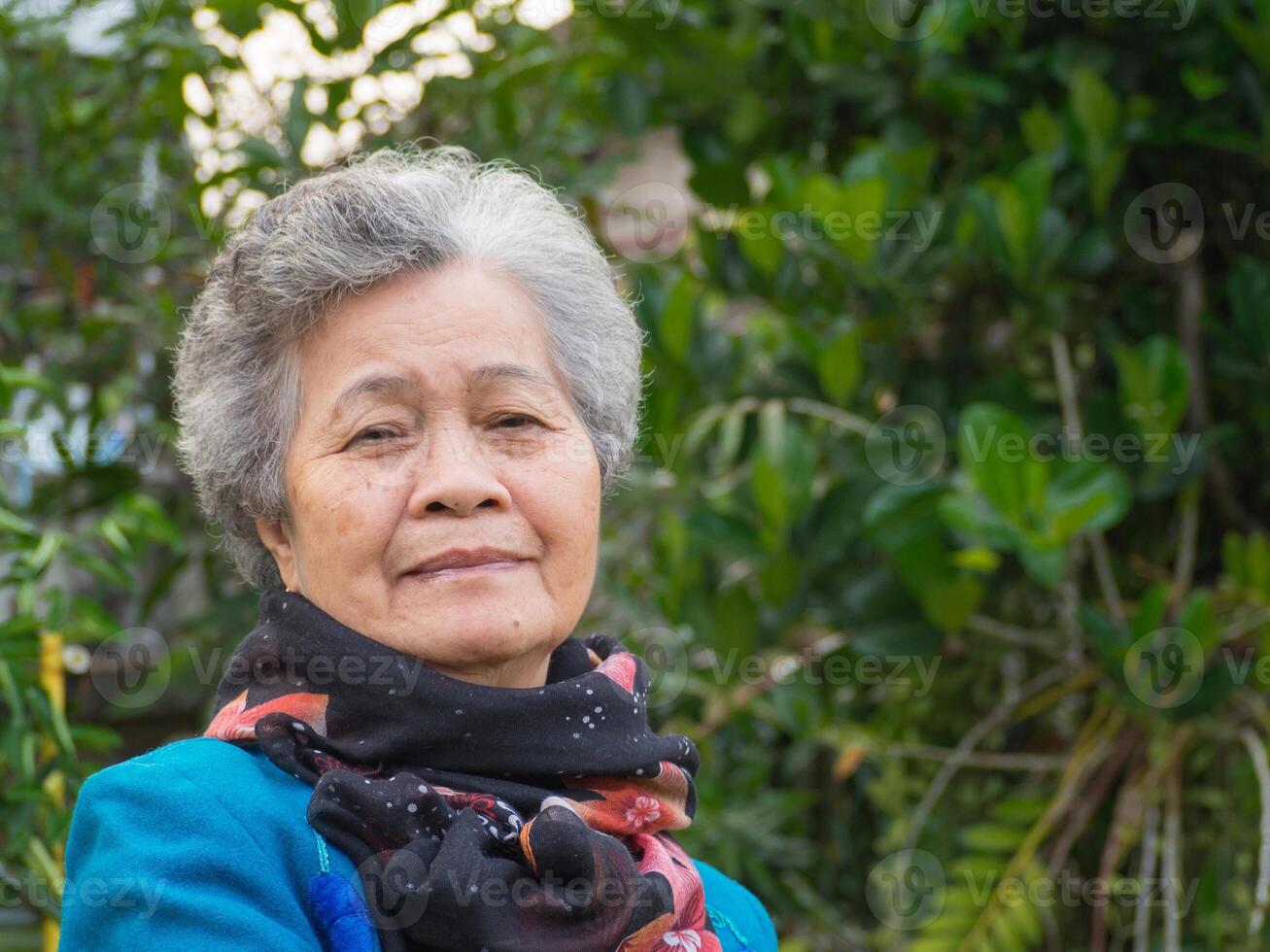 Senior woman smiling and looking at the camera while standing in a garden. Headshot photo. Concept of aged people and healthcare photo