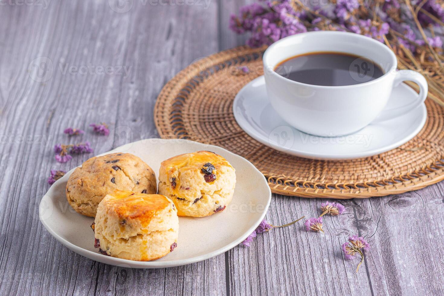 Traditional British scones and cookies on a plate with a white coffee cup and flower blurred background. Close-up photo with copy space for text