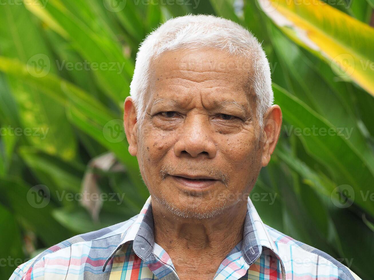 Portrait of an elderly Asian man smiling and looking at the camera while standing in a garden. Concept of aged people and healthcare photo