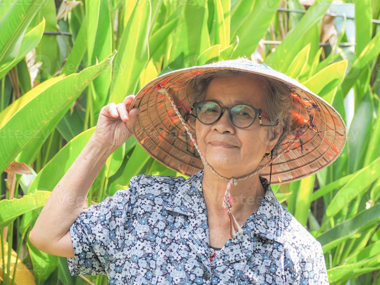 Portrait of a senior Asian woman wearing a hat, smiling and looking at the camera while standing in a garden. Space for text. Concept of old people and healthcare photo