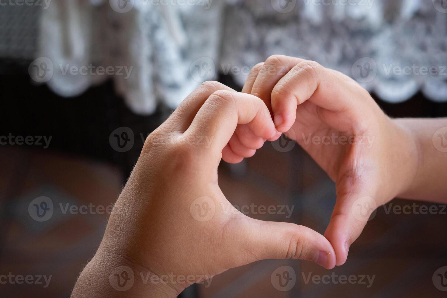 Close-up photo of hands a child making fingers showing as a heart symbol to say that I love you. The heart shape tells the love feel romantic that is given to each other. Valentine's day