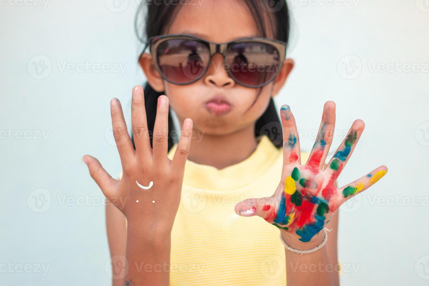 Cute little girl with colorful painted hands on wall background photo