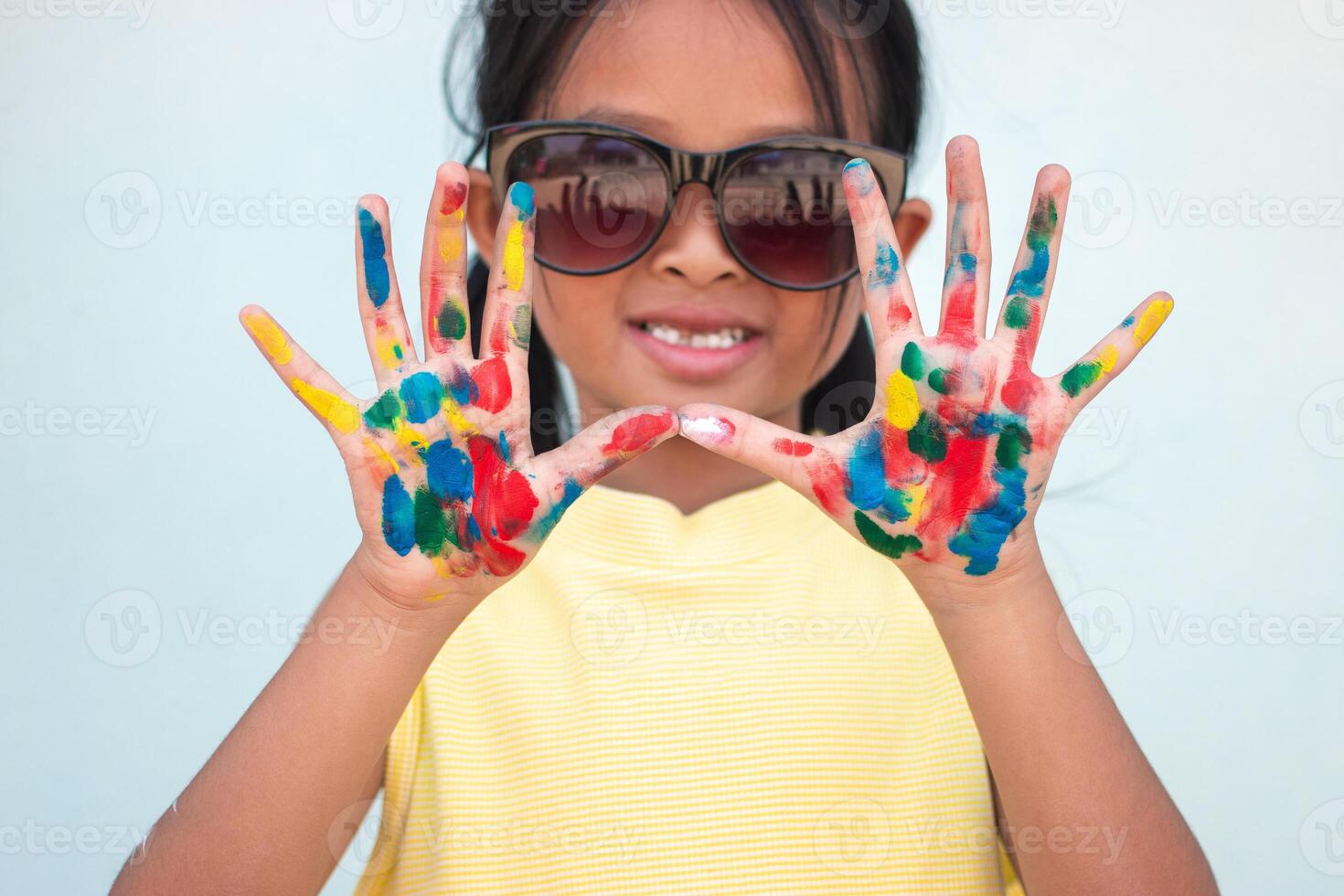 Cute little girl with colorful painted hands on wall background photo