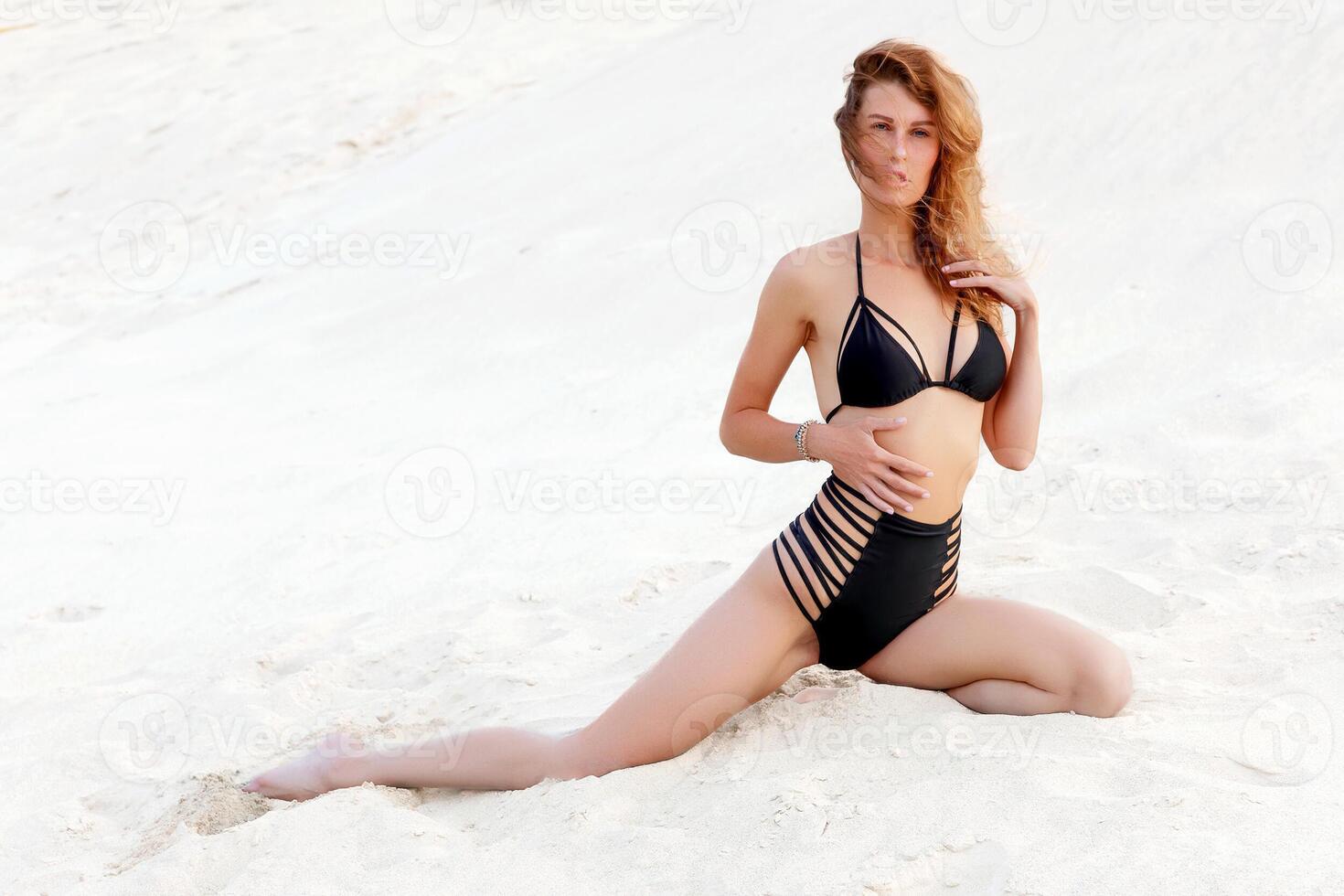 retrato de joven mujer en negro traje de baño relajante en arenoso playa foto