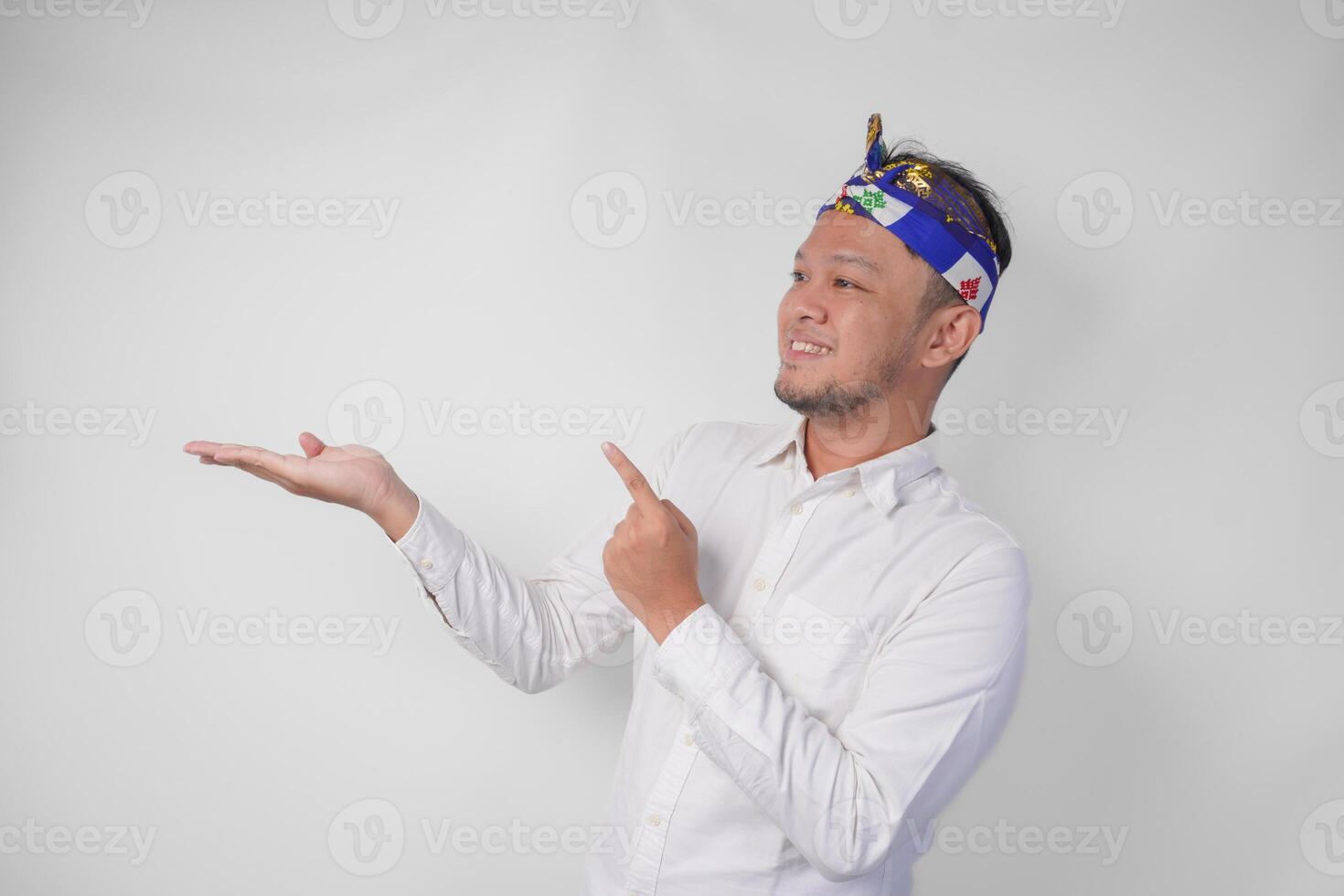 Attractive Balinese man in white shirt and traditional headdress called udeng pointing to the copy space on the left and right side while smiling cheerfully photo