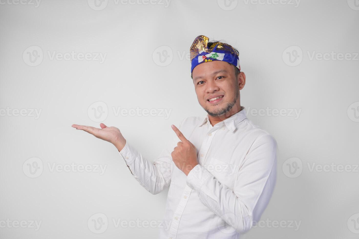 Attractive Balinese man in white shirt and traditional headdress called udeng pointing to the copy space on the left and right side while smiling cheerfully photo