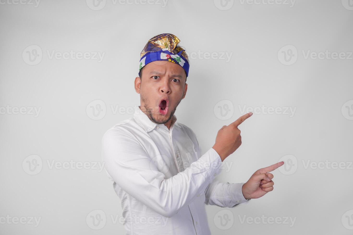 sorprendido balinés hombre en blanco camisa y tradicional tocado llamado udeng señalando a el Copiar espacio en el izquierda y Derecha lado foto