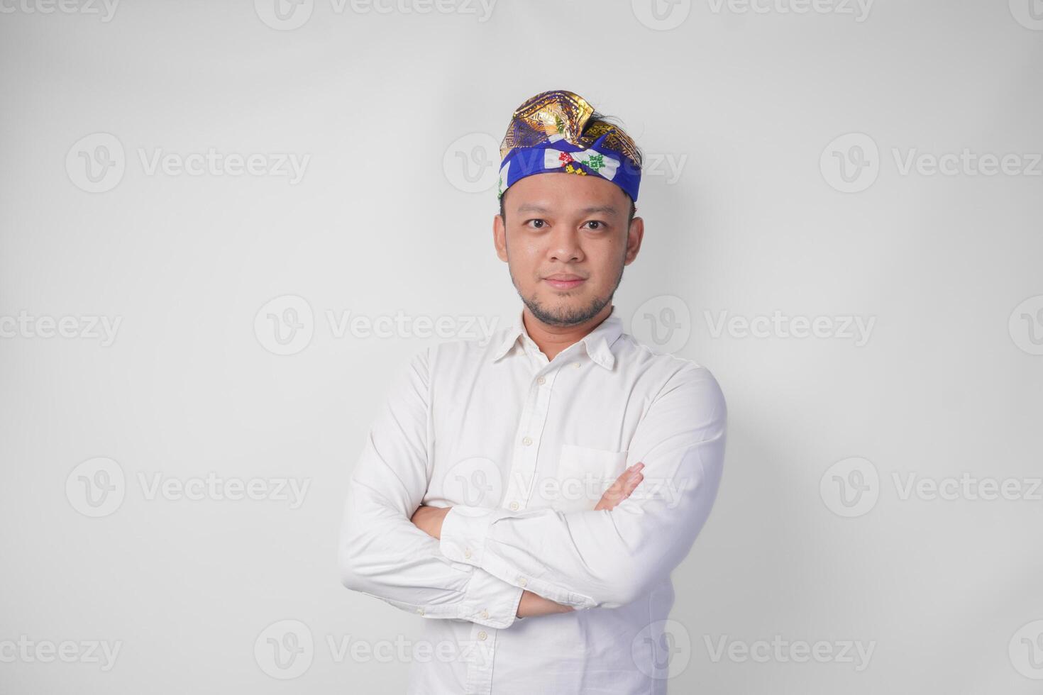 retrato de un balinés vistiendo tradicional tocado llamado udeng posando con un cruzado brazos y confidente sonrisa terminado aislado blanco antecedentes foto