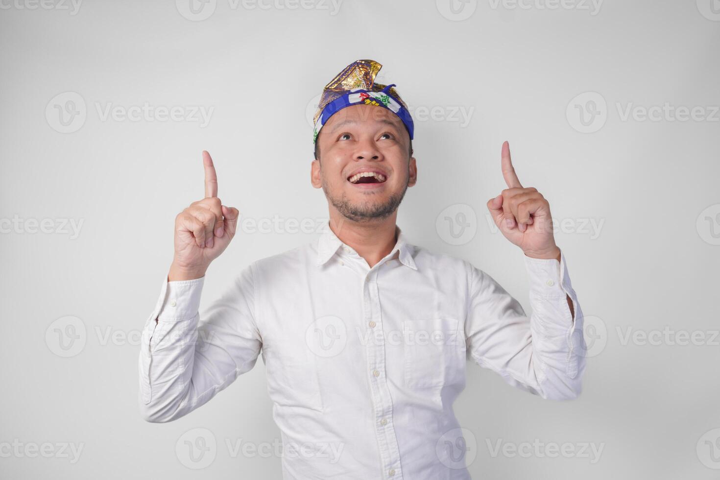 Surprised Balinese man wearing traditional headdress called udeng pointing up to the copy space upwards over isolated white background photo