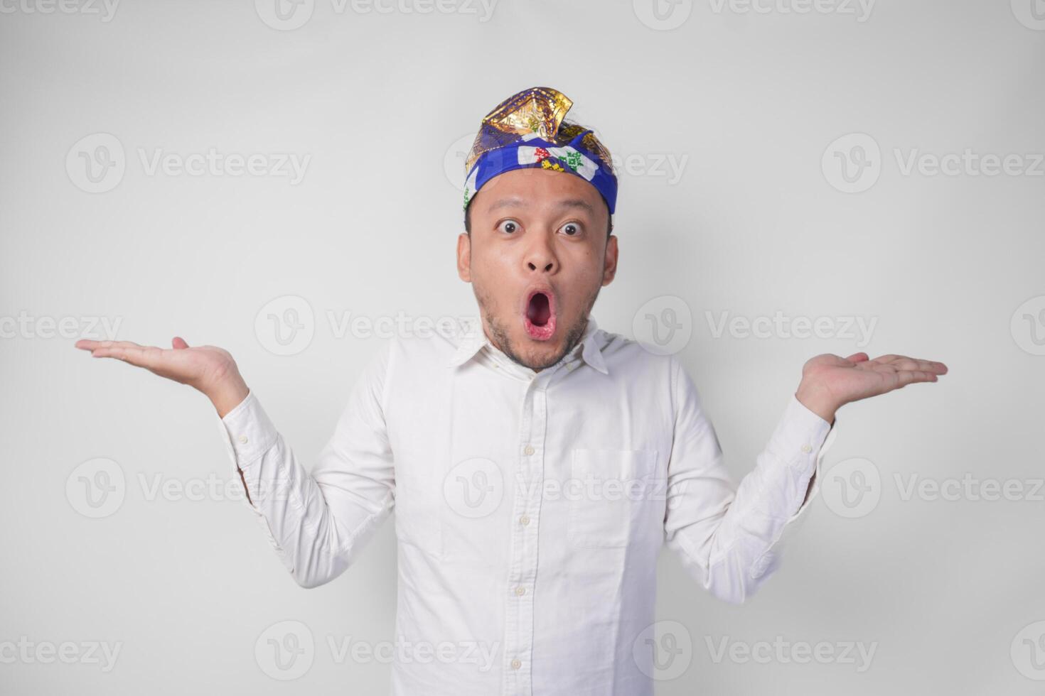 Surprised Balinese man in white shirt and traditional headdress called udeng pointing to the copy space on the left and right side photo