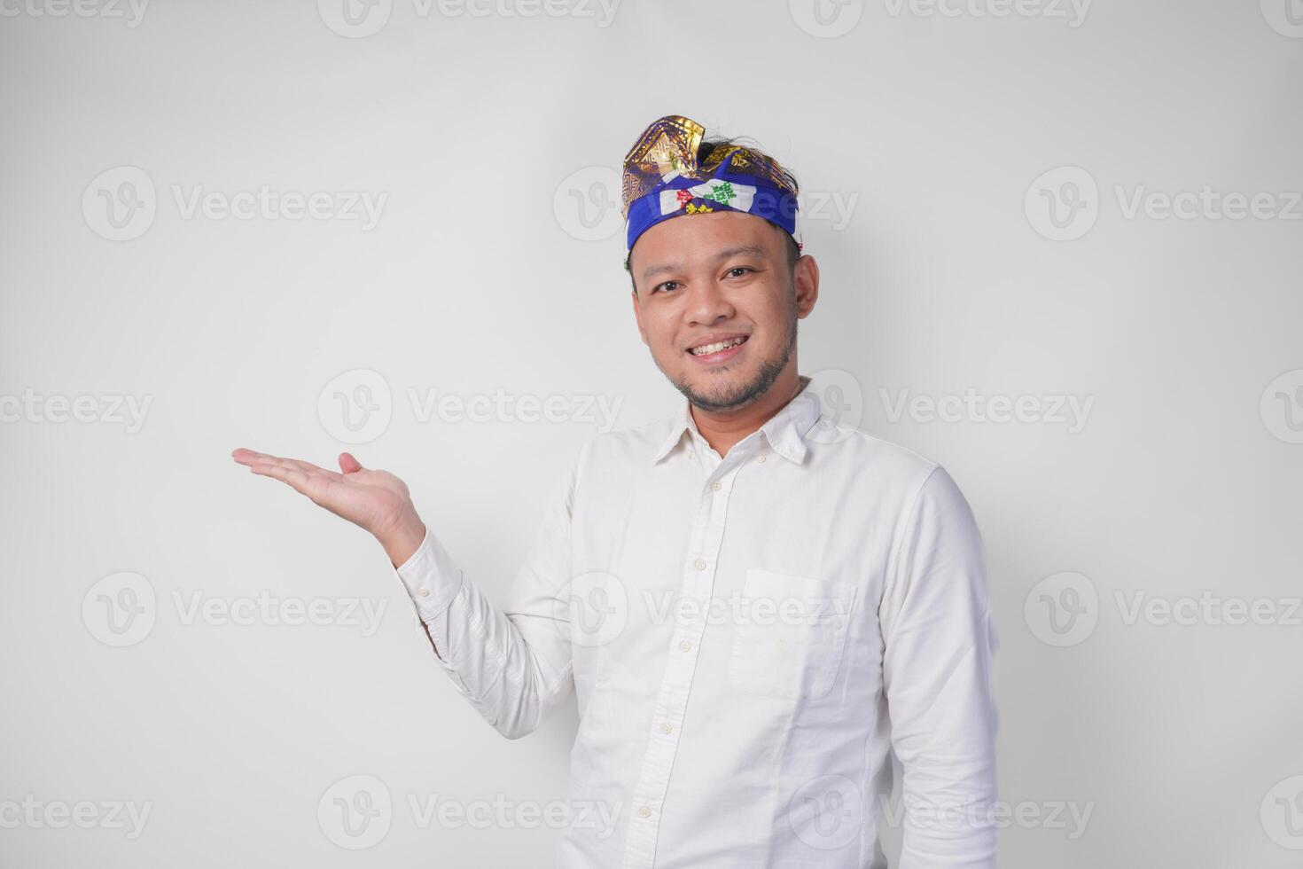 Attractive Balinese man in white shirt and traditional headdress called udeng pointing to the copy space on the left and right side while smiling cheerfully photo