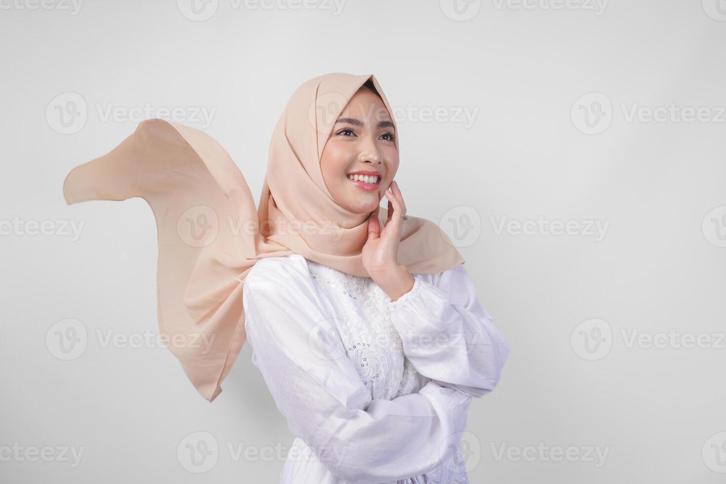 Elegant young Asian Muslim woman wearing white dress with hijab waving in the wind, modelling pose on white background photo