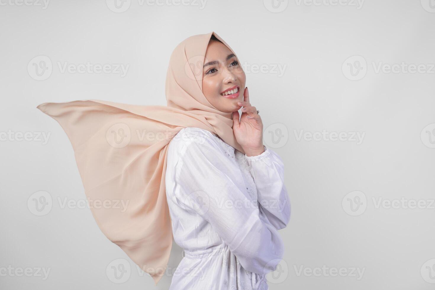 Elegant young Asian Muslim woman wearing white dress with hijab waving in the wind, modelling pose on white background photo