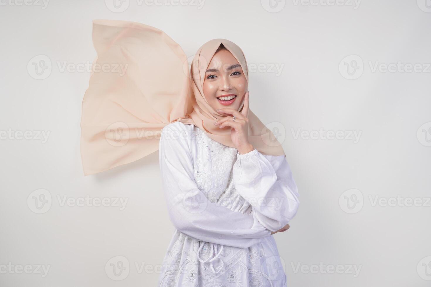 Elegant young Asian Muslim woman wearing white dress with hijab waving in the wind, modelling pose on white background photo