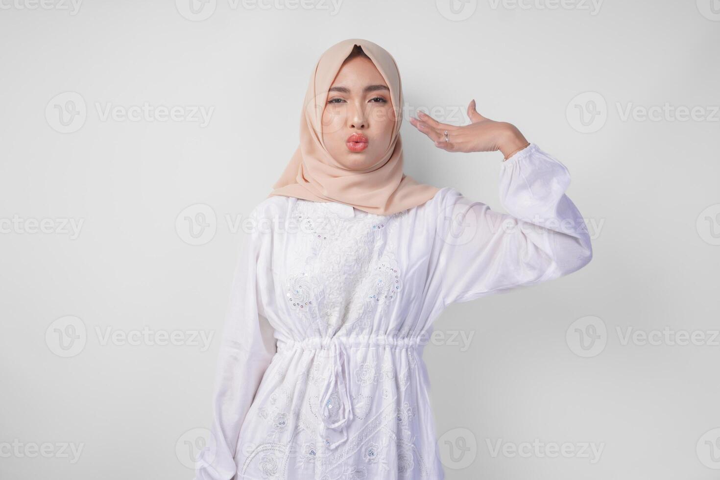 Young Asian Muslim woman in white dress and hijab raising hand to fan herself feeling hot due to summer weather while fasting. Ramadan concept photo
