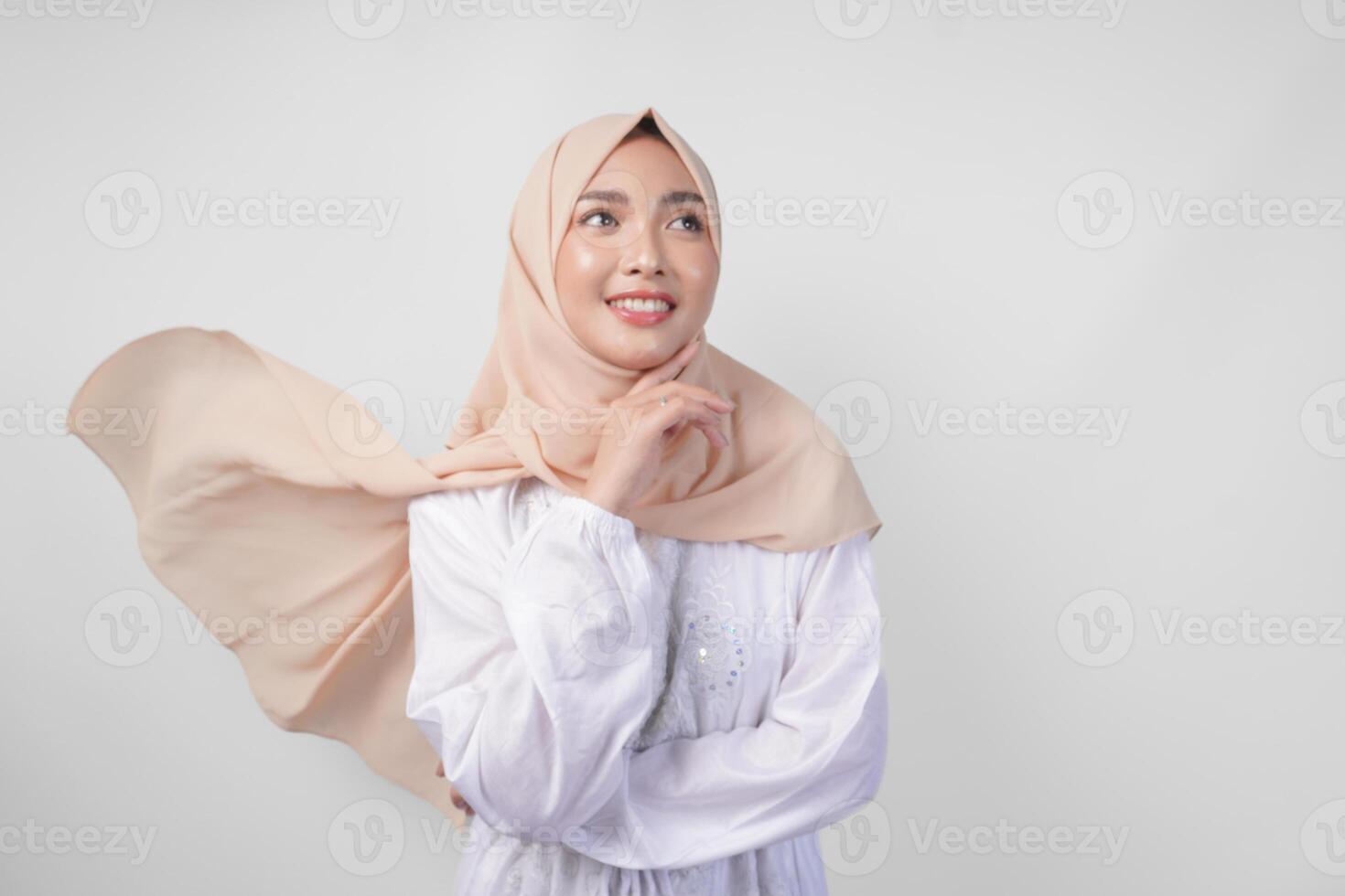 Elegant young Asian Muslim woman wearing white dress with hijab waving in the wind, modelling pose on white background photo