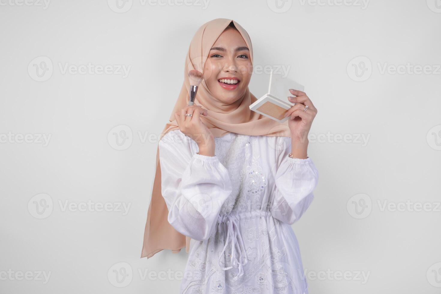 hermosa joven asiático musulmán mujer vistiendo blanco vestir y hijab aplicando hacer arriba utilizando cepillar. Moda y productos cosméticos belleza concepto foto