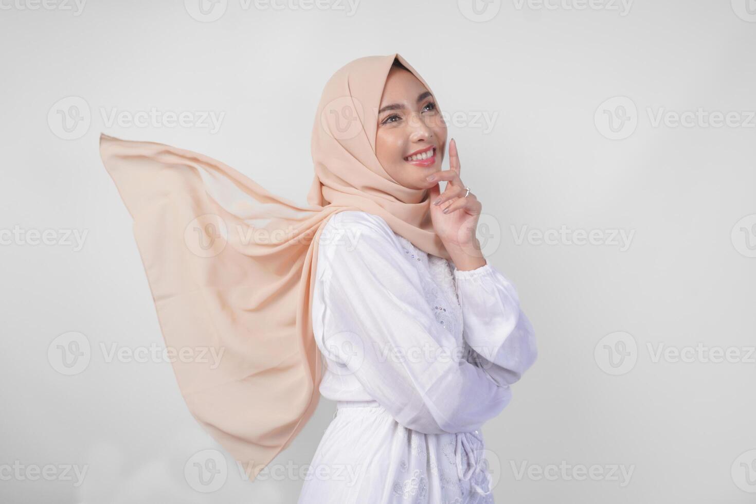 Elegant young Asian Muslim woman wearing white dress with hijab waving in the wind, modelling pose on white background photo