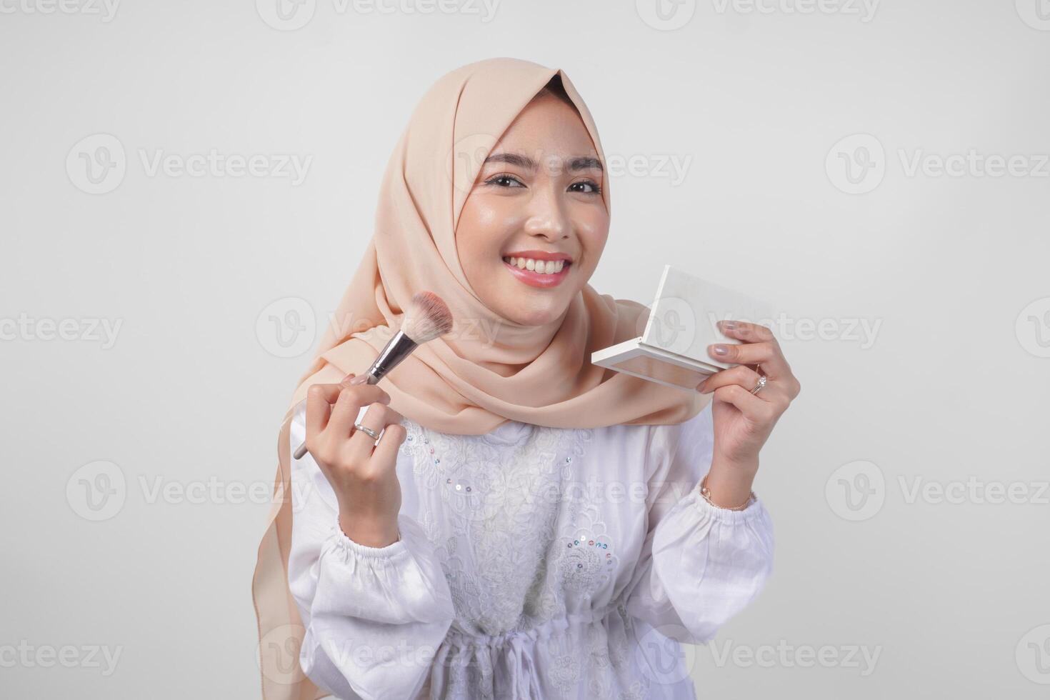 hermosa joven asiático musulmán mujer vistiendo blanco vestir y hijab aplicando hacer arriba utilizando cepillar. Moda y productos cosméticos belleza concepto foto