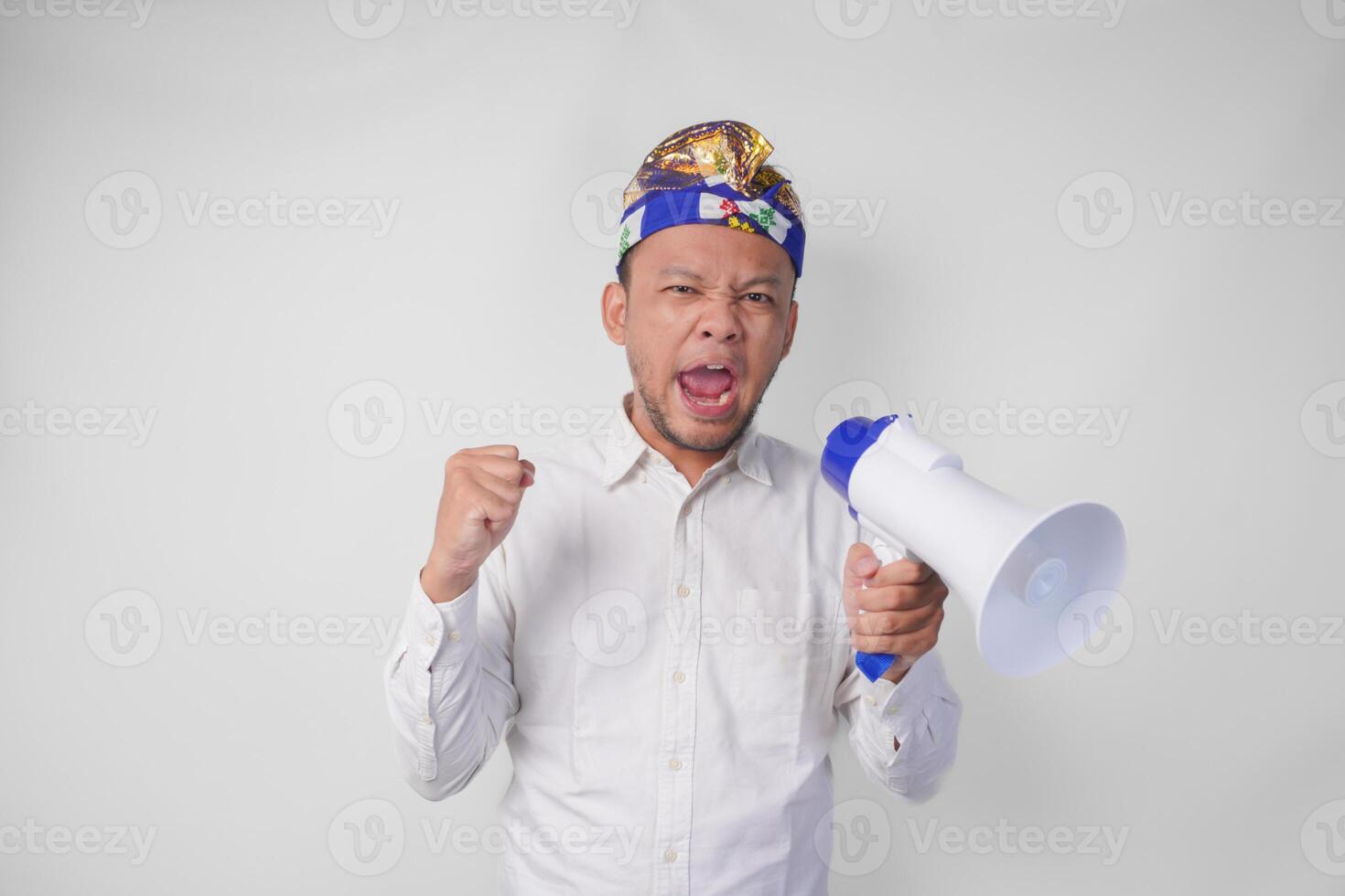 lleno de alegría balinés hombre en blanco camisa y tradicional tocado gritos a megáfono sensación entusiasmado, aislado por blanco antecedentes foto